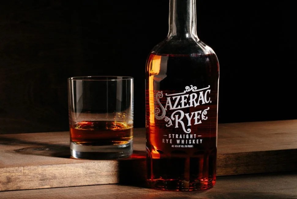 A bottle of Sazerac Rye on a wooden table next to a poured glass of Rye