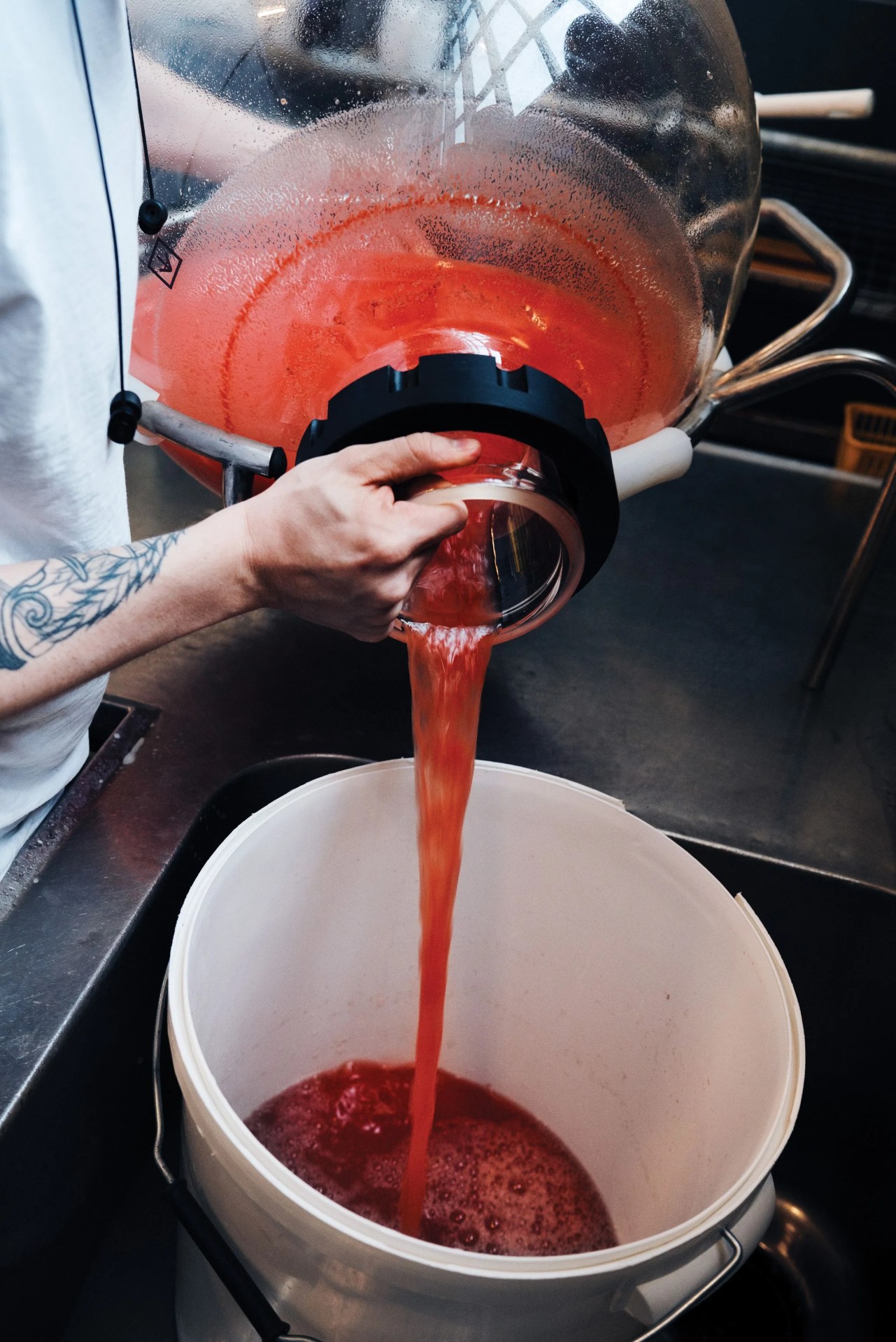 man pouring red liquid from a glass container into a bucket