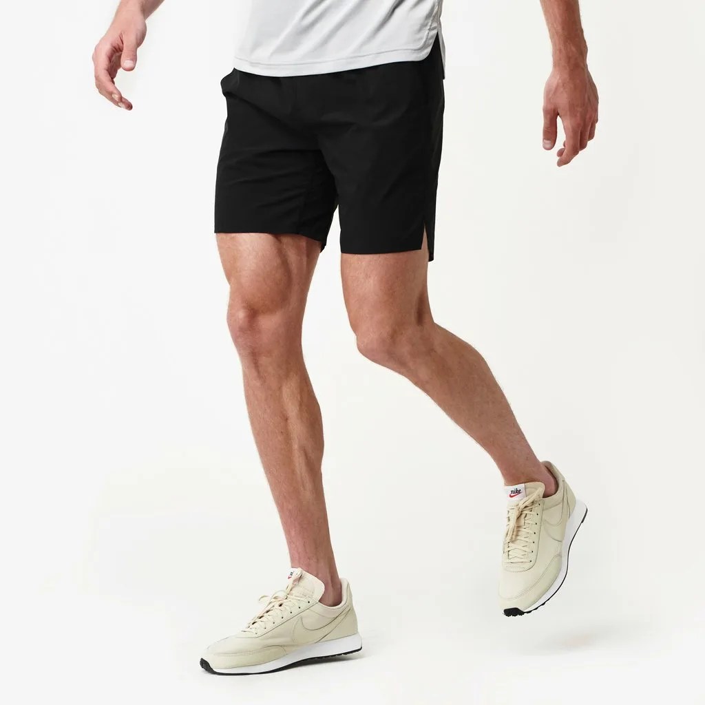 A pair of black shorts on a model with white sneakers on a gray background.