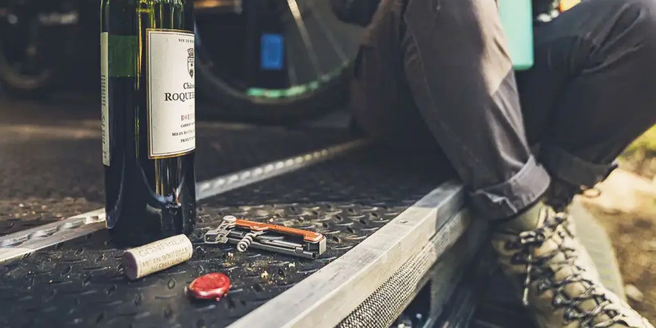 a multi tool with an orange handle and corkscrew next to an open bottle of wine