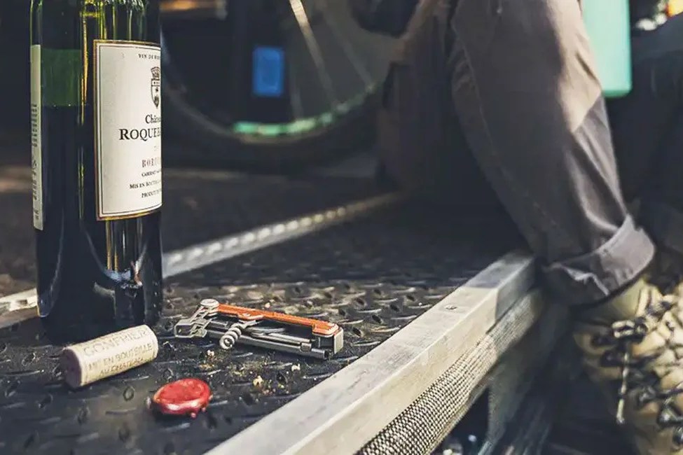 a multi tool with an orange handle and corkscrew next to an open bottle of wine