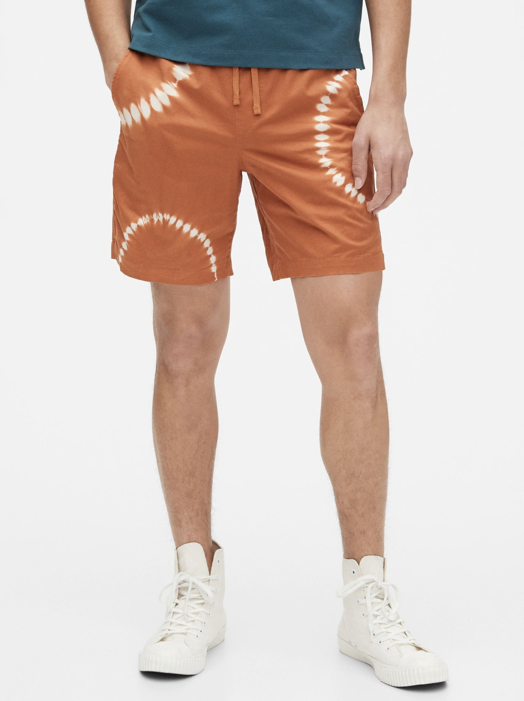 A model wearing orange tie dye shorts on a gray background.