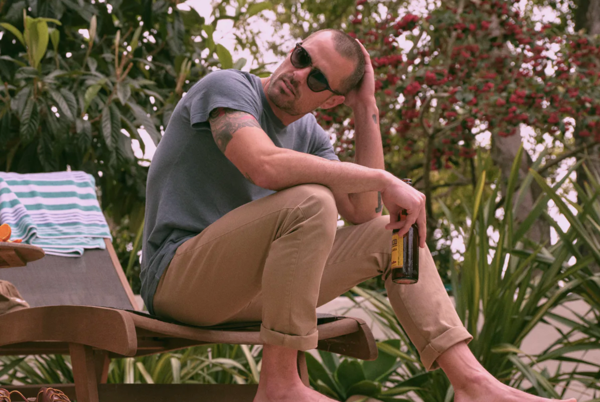 a model sitting by a pool with a beer, khakis and a gray t shirt