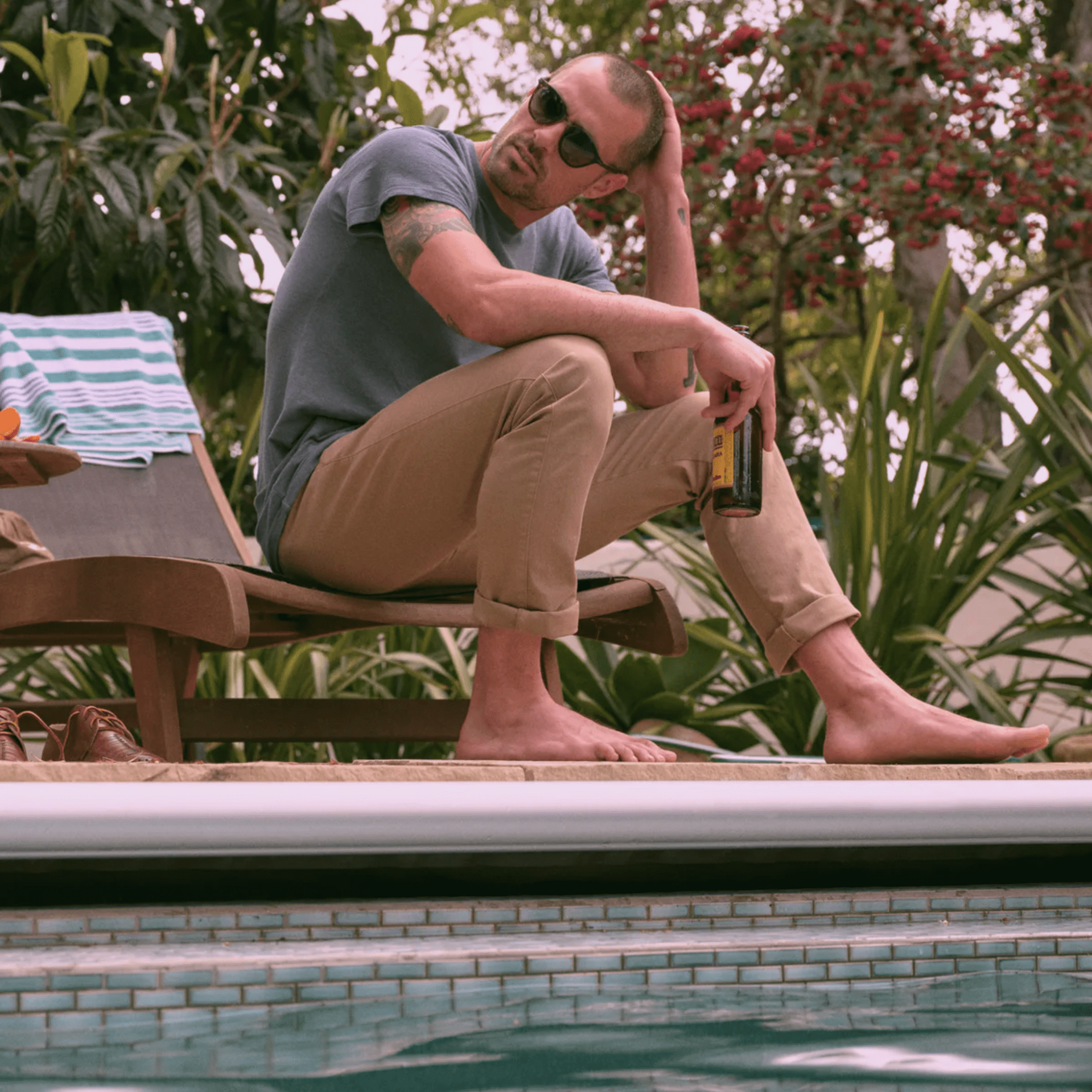 a model sitting by a pool with a beer, khakis and a gray t shirt