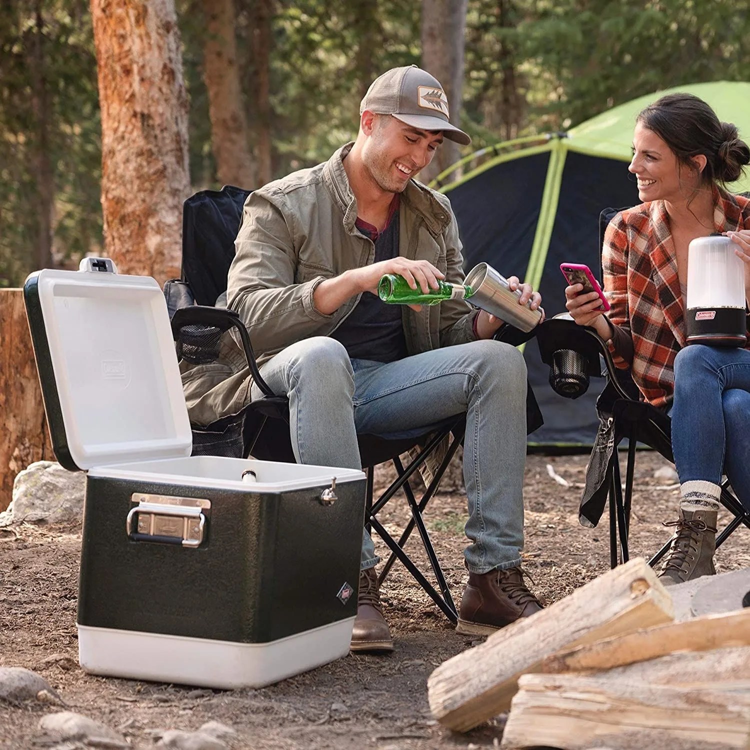 a campsite with a cooler, logs, a couple in camping chairs and a tent