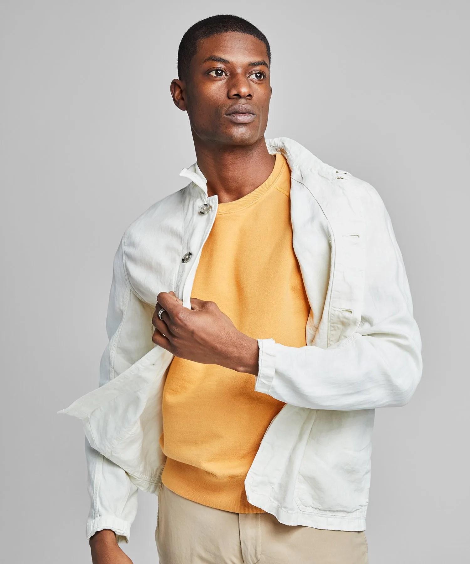 A model wearing a white chore coat, yellow shirt and khakis.