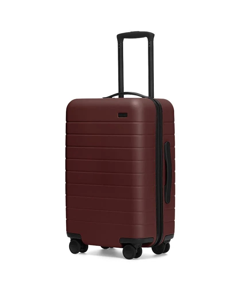 A red carry-on rolling suitcase on a gray background.