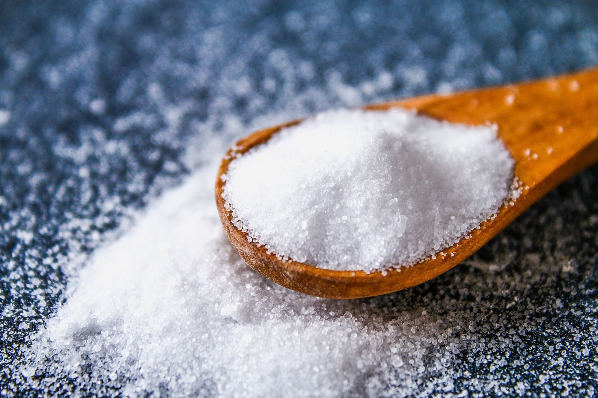 crystals of shallow salt in a scoop, spoon on a dark gray table background for advertising salt table salty salted food
