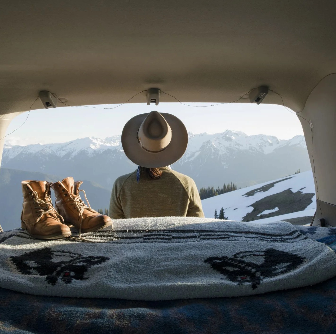 rear view of female hiker looking at snowcapped mountains while standing outside sports utility vehicle