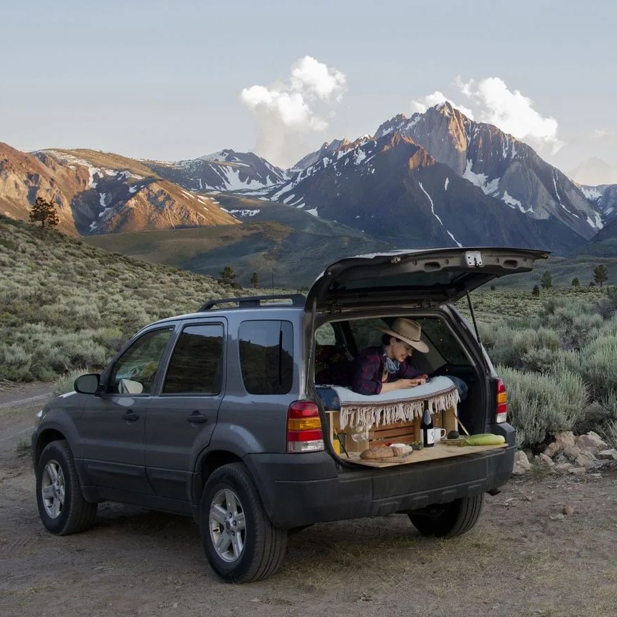 female hiker sitting in sports utility vehicle against mount morrison
