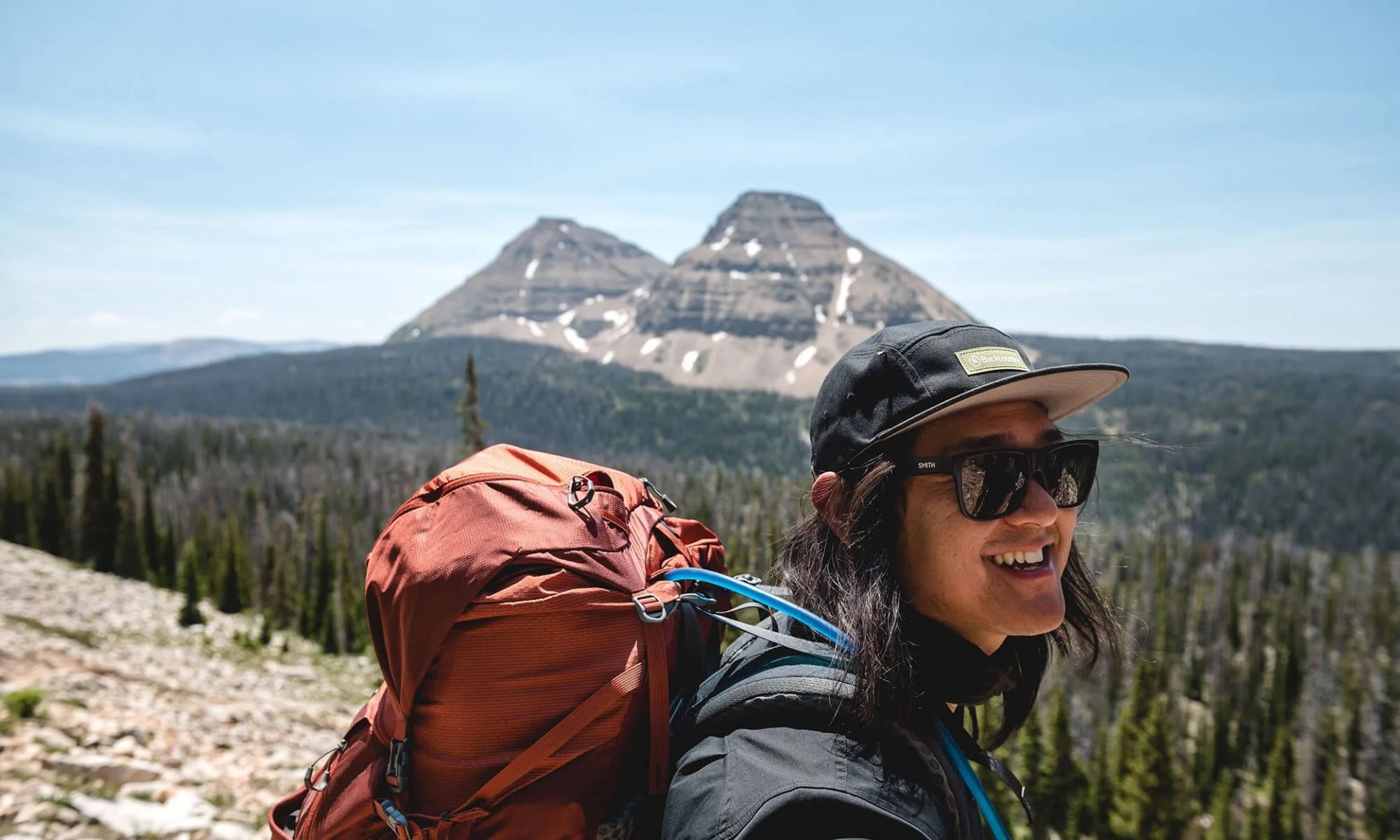 person smiling wearing backcountry gear in front of mountain
