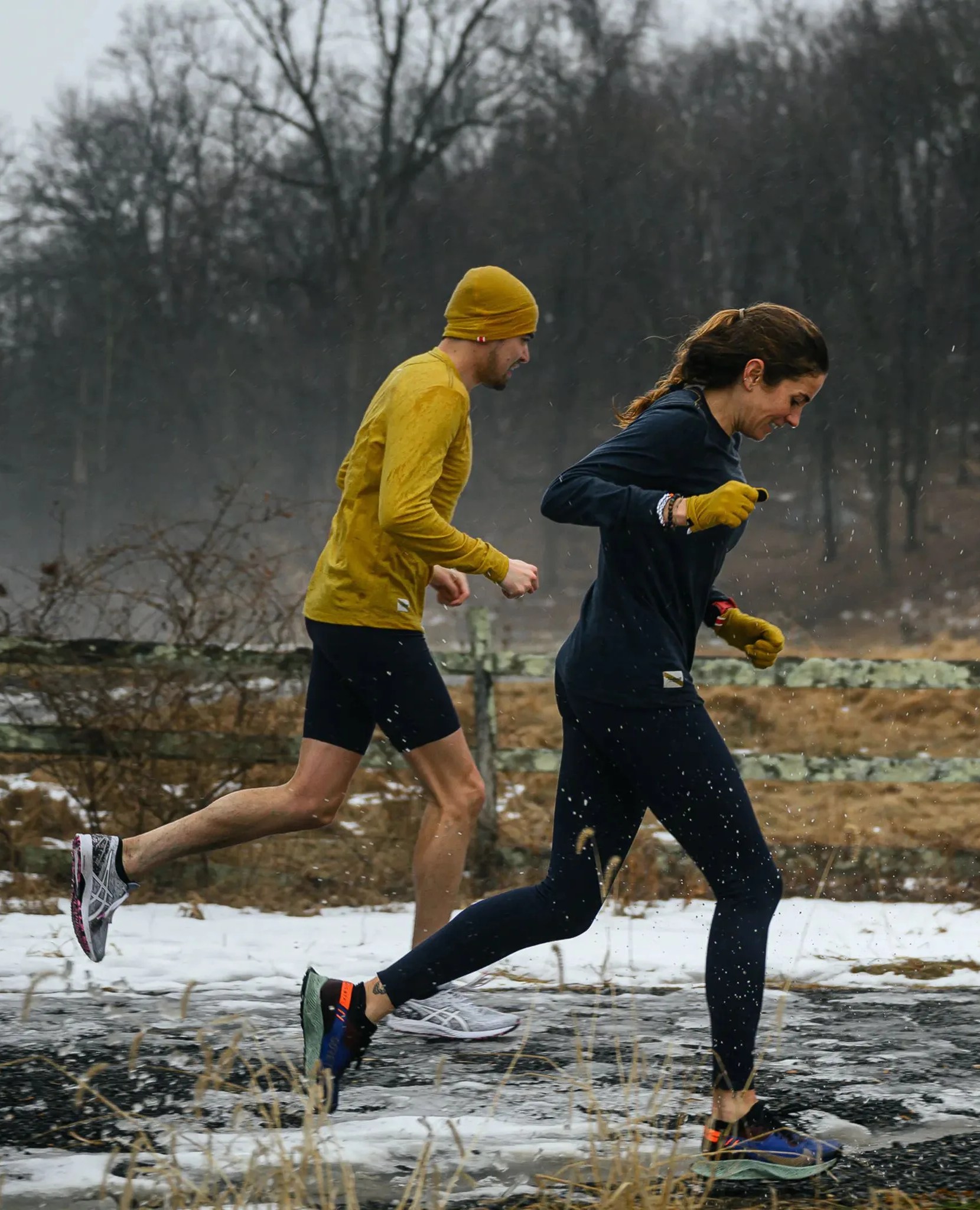 man and woman running in snowy street wearing the tracksmith's the thaw collection