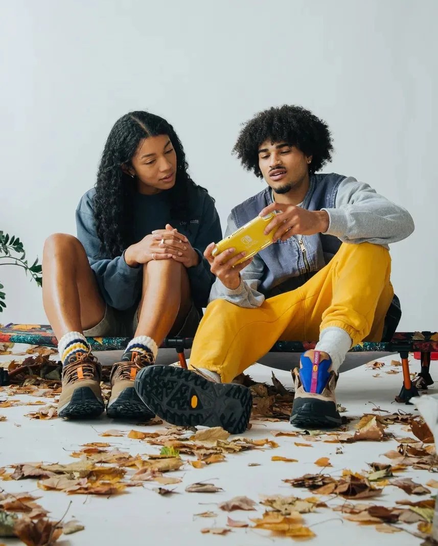two people sitting on bodega x helinox convertible cot