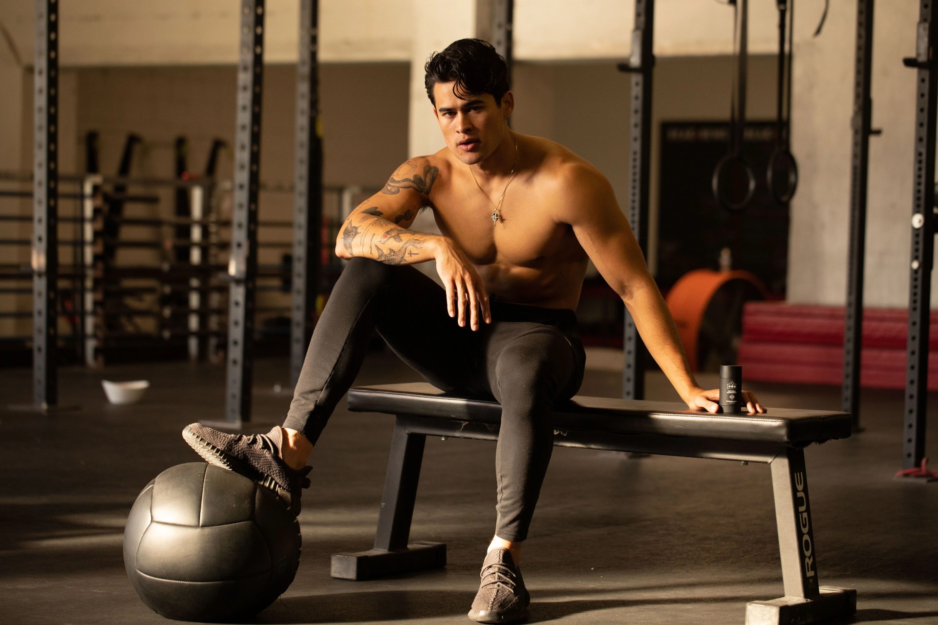 shirtless man sitting on workout bench with leg propped up on a ball holding hardworking gentlemen product