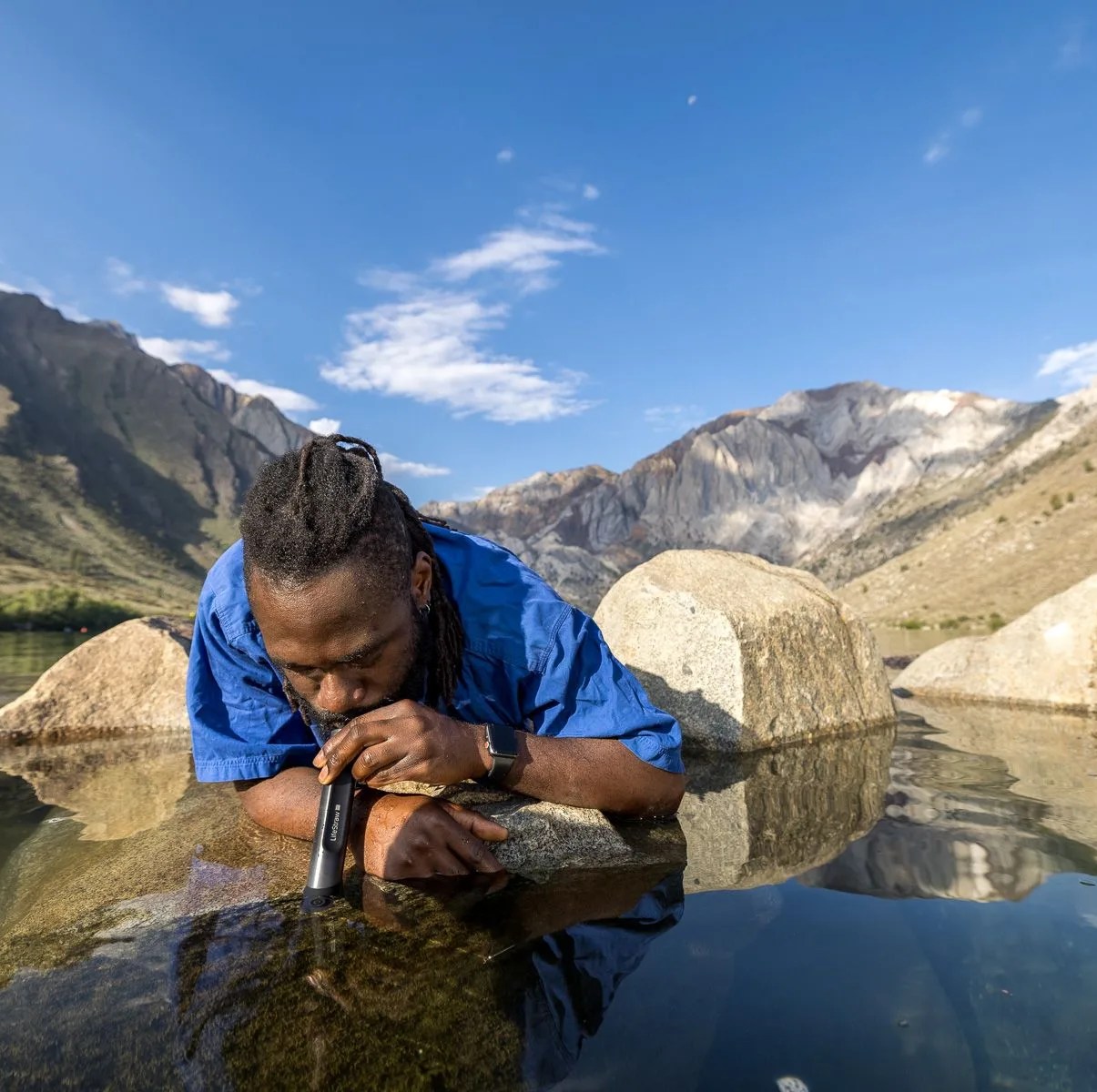 man drinking out of lifestraw from lake