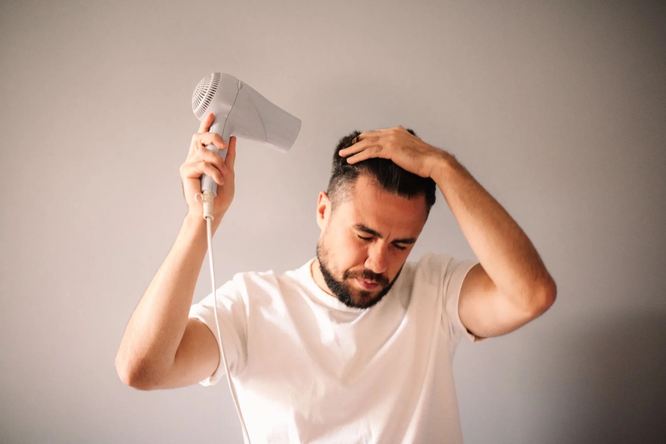 man blow drying hair against gray wall at home