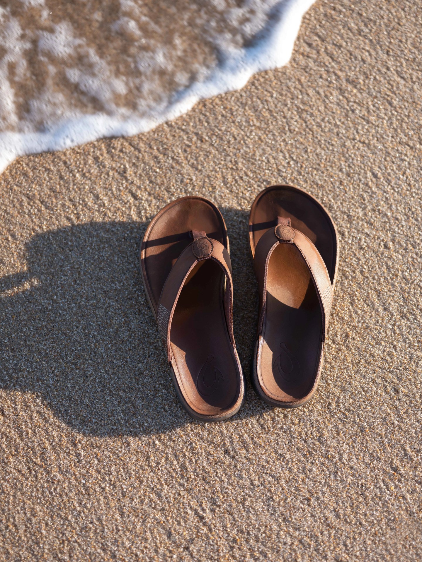 olukai tuahine sandals on beach with tide coming in