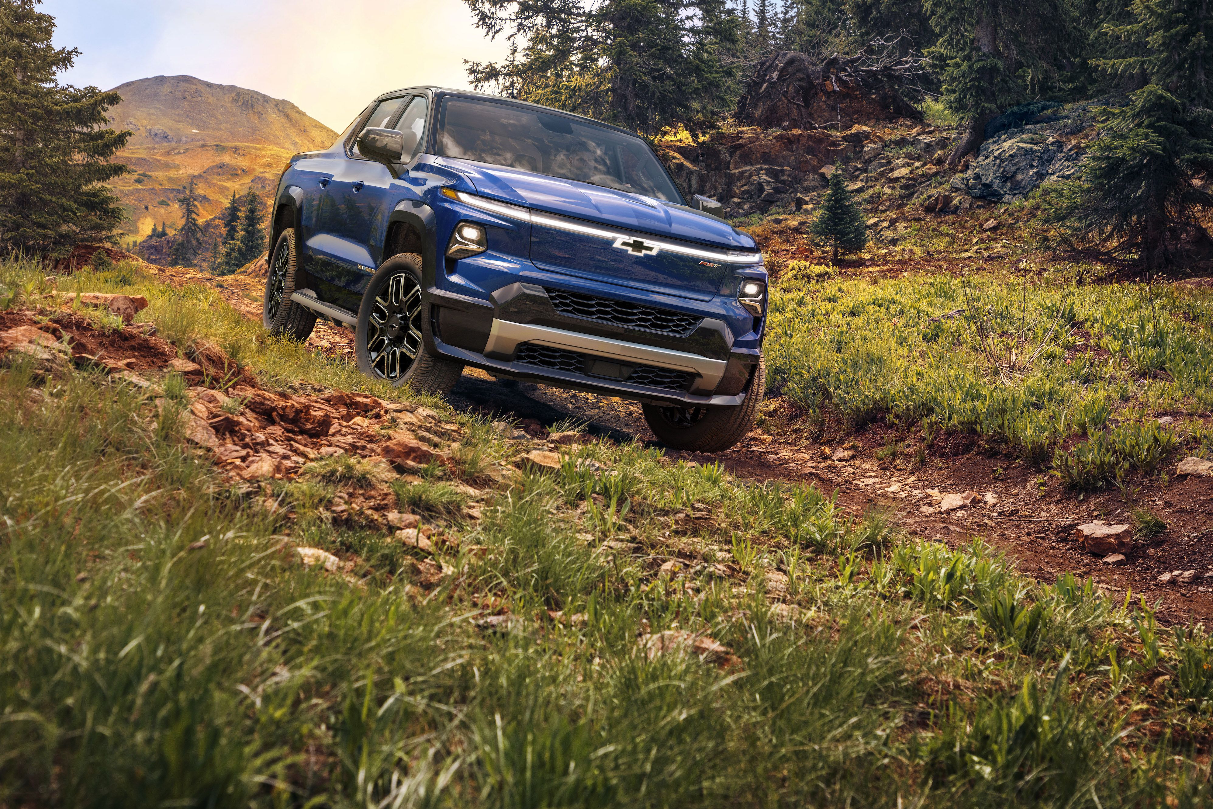 chevrolet 2024 silverado ev driving on a wooded path with trees and mountains in the background