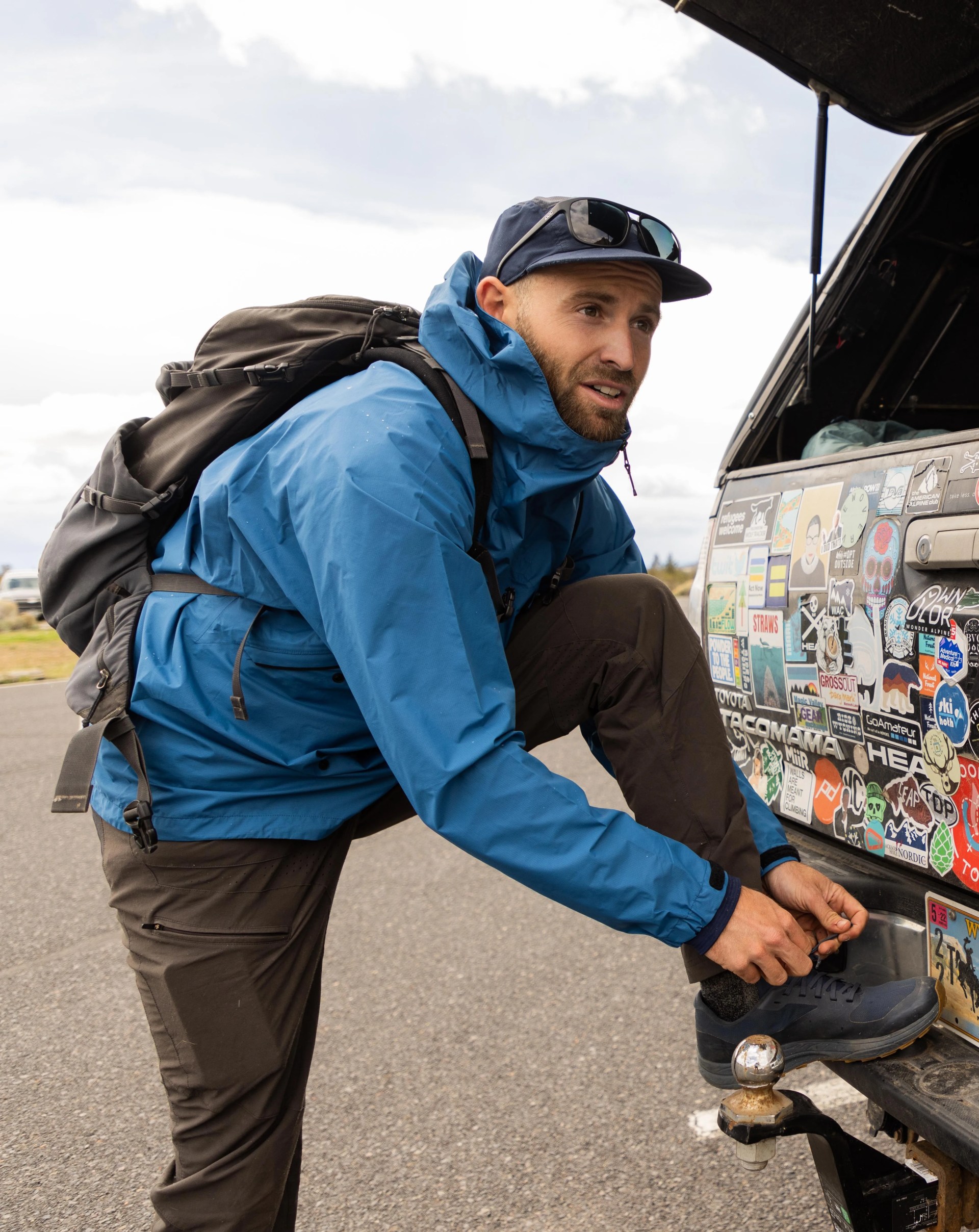 andy cochrane bent down with his left leg propped on car bumper to tie shoe