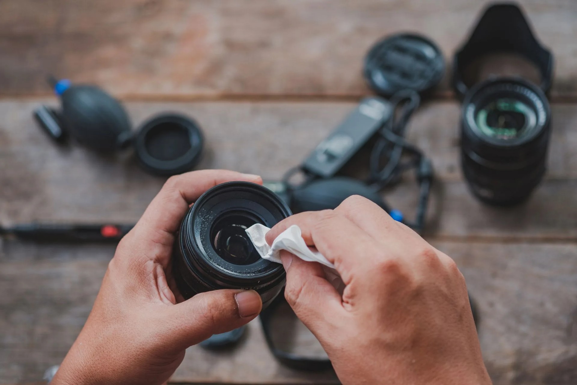 cropped hands of man cleaning camera lens on table