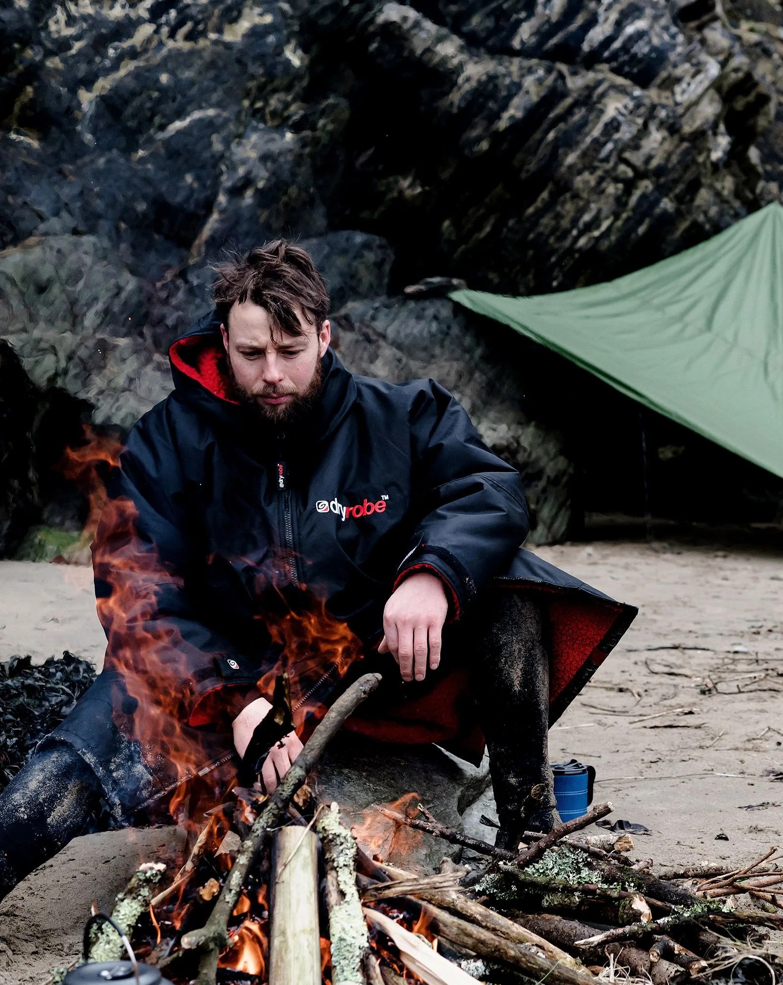 man wearing dryrobe® sitting by the fire on beach