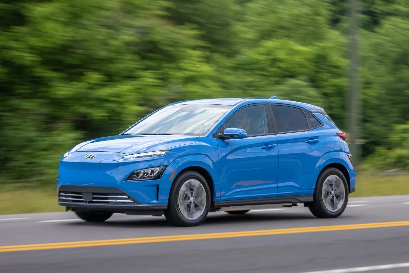 side profile of hyundai kona electric driving on the road with a forest in the background