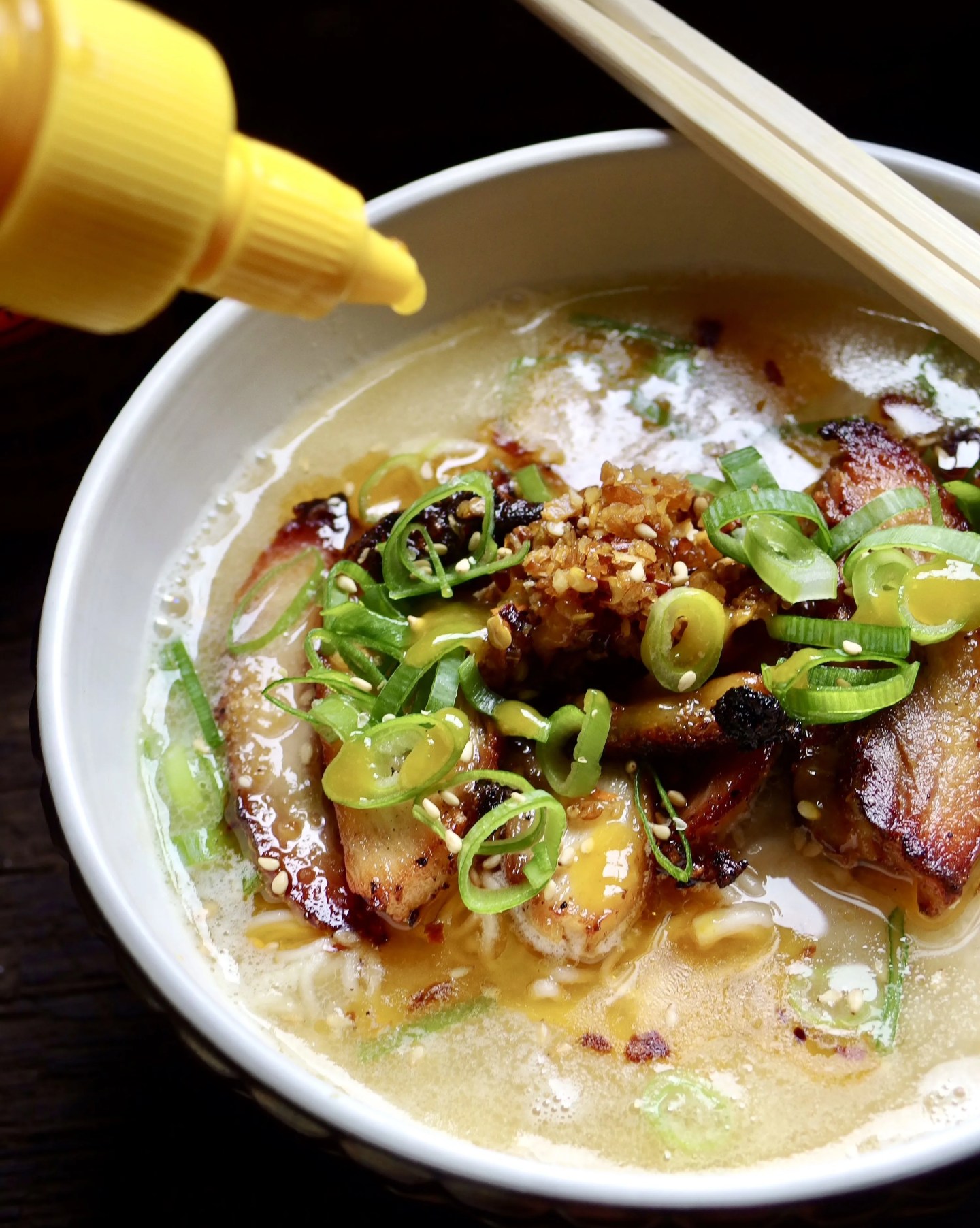 yellow sriracha being squirted onto a bowl of noodles