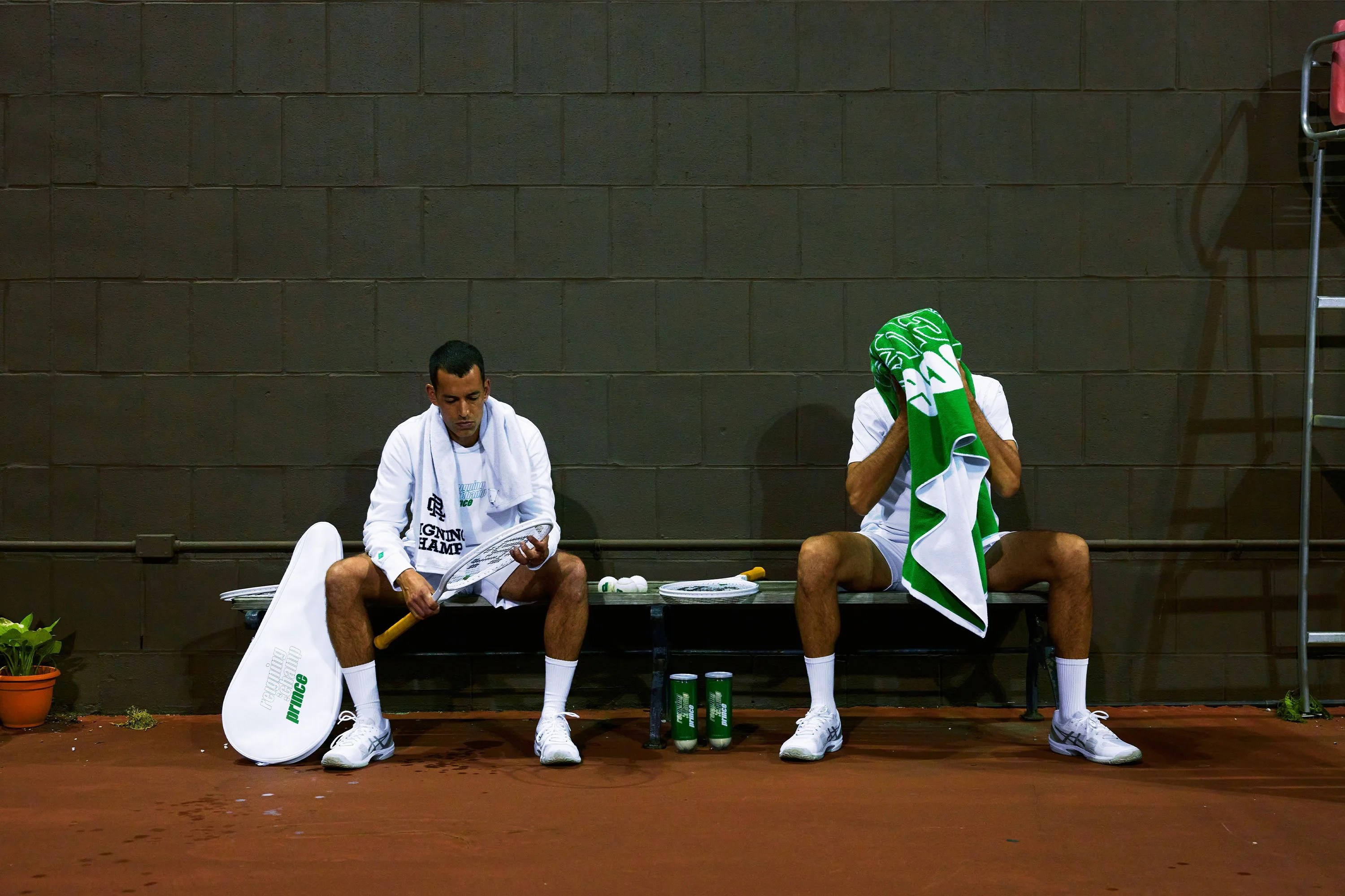 two men sit on a bench with tennis rackets