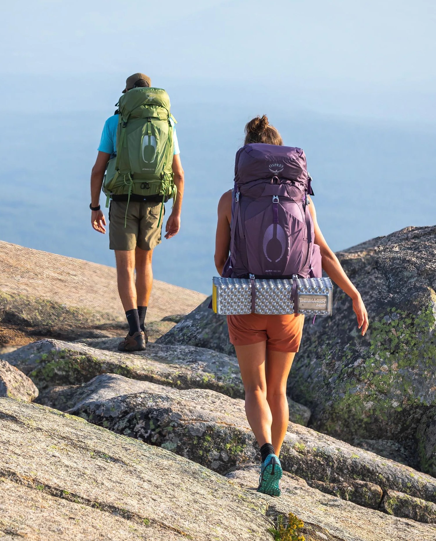 two people walking along rocky cliff wearing osprey atmos aura backpack