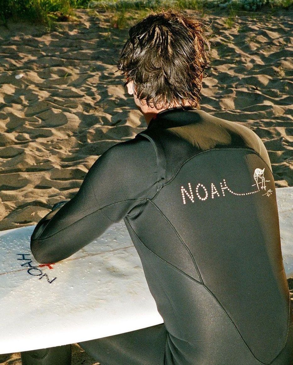 man wearing noah's sustainable wetsuit leaning on surfboard