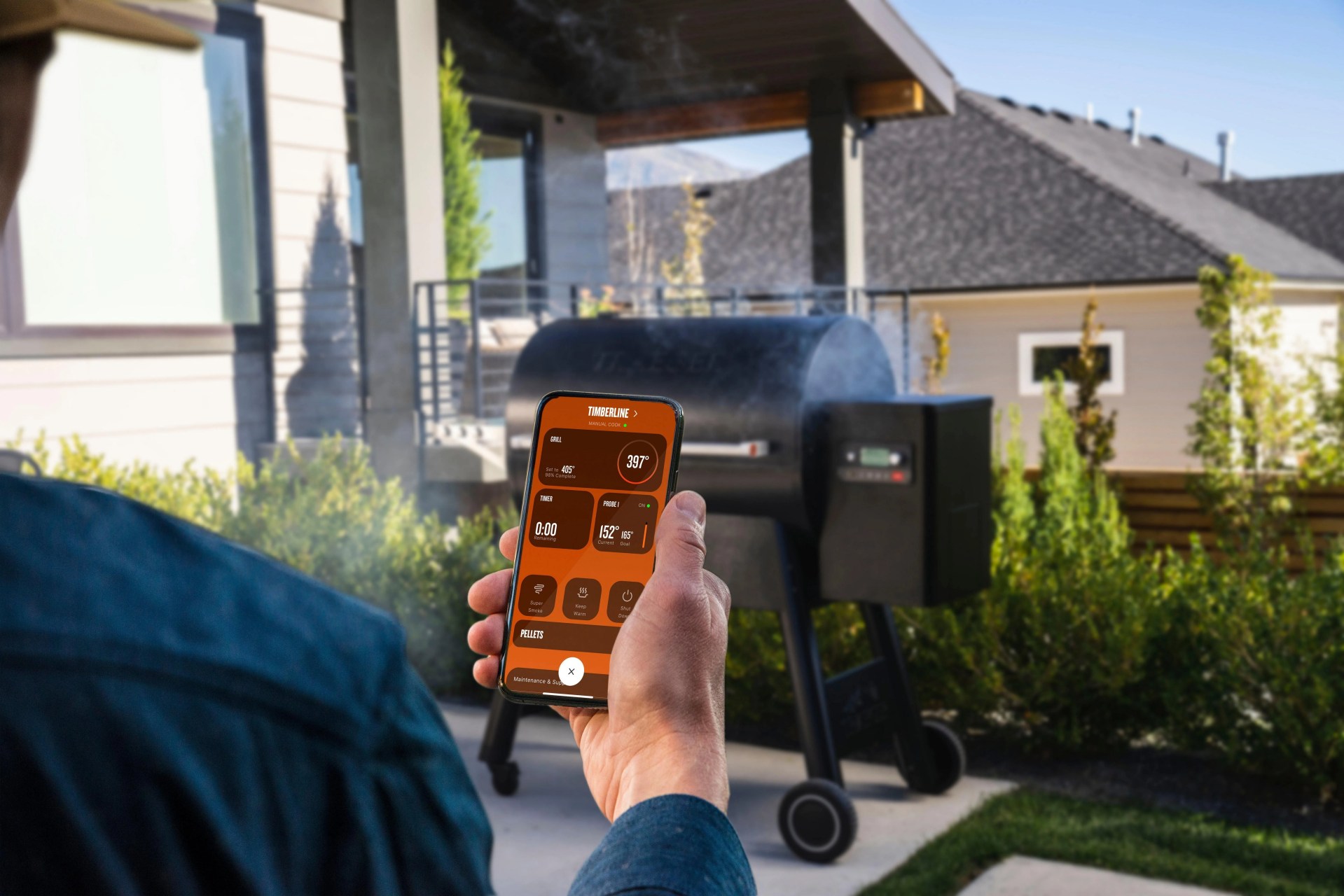 person looking at their phone screen to monitor their traeger grill