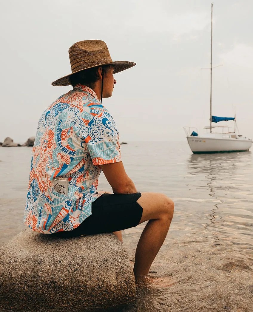 man wearing california cowboy apparel sitting on rock by water
