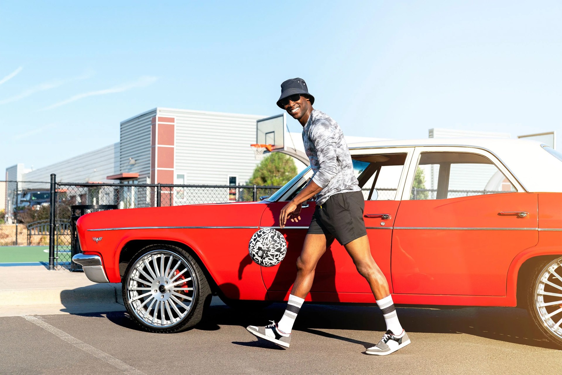 man bouncing a basketball next to a red convertible car