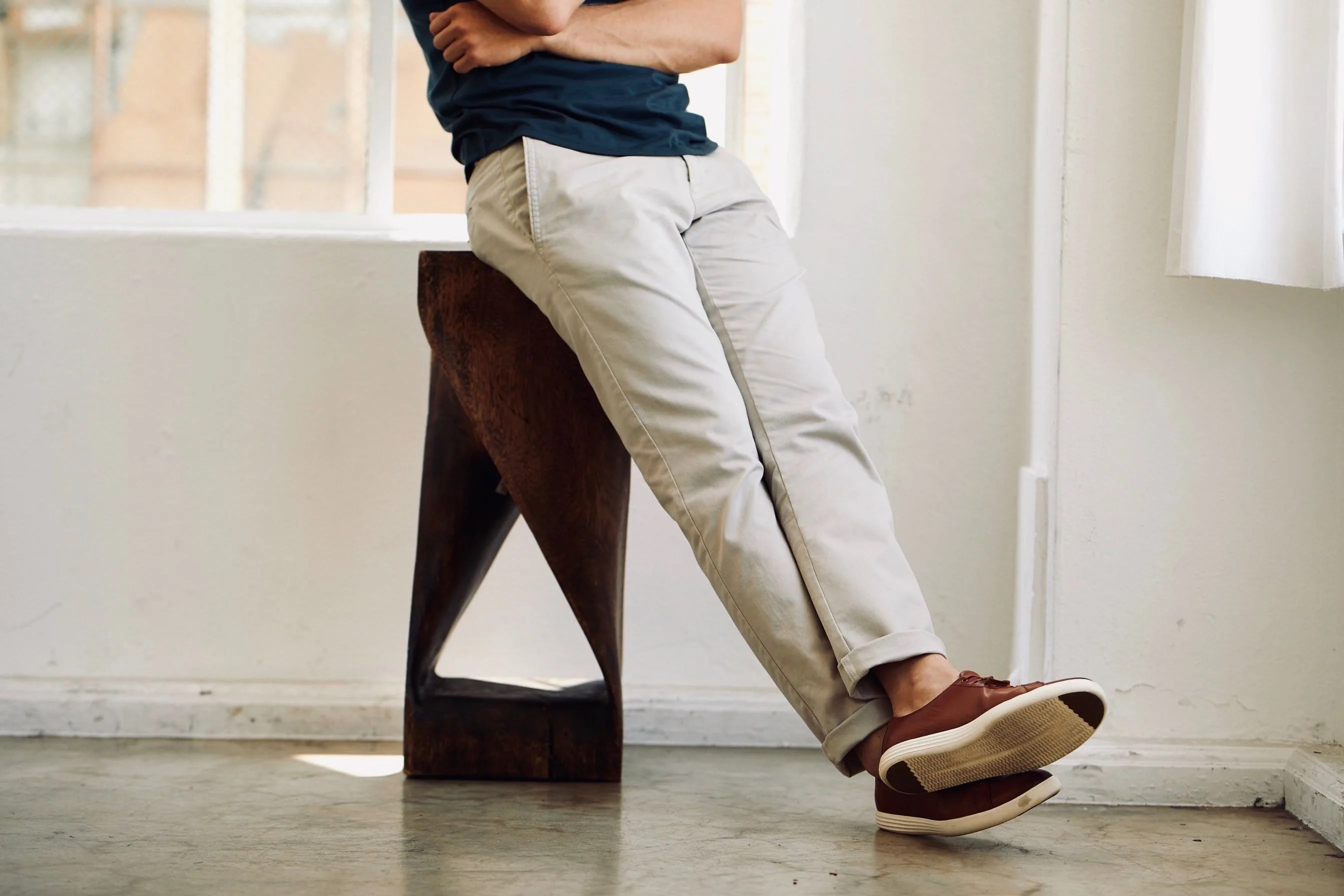 man learning against stool with arms crossed wearing perk clothing chinos