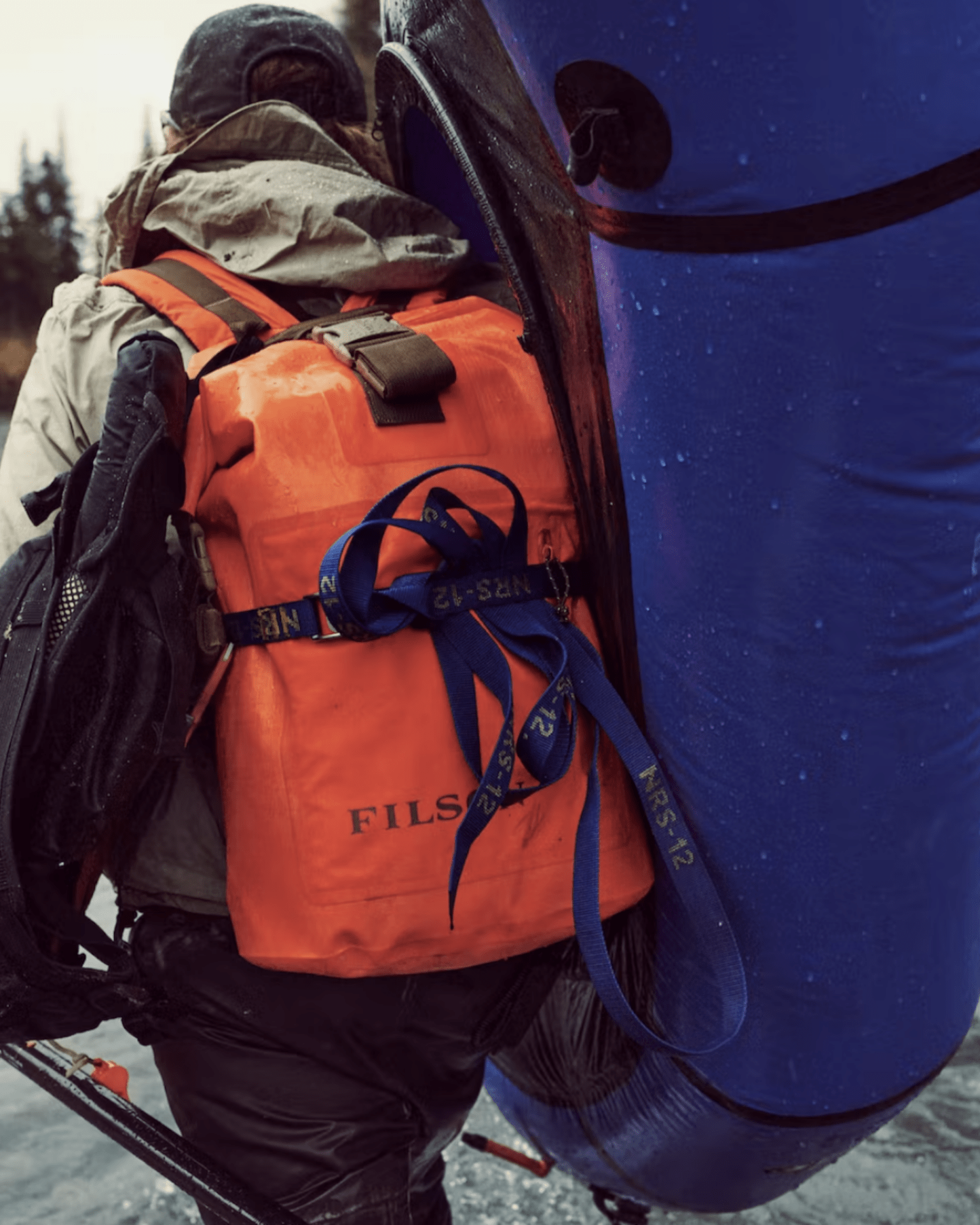 a man wearing an orange filson dry backpack in wet conditions