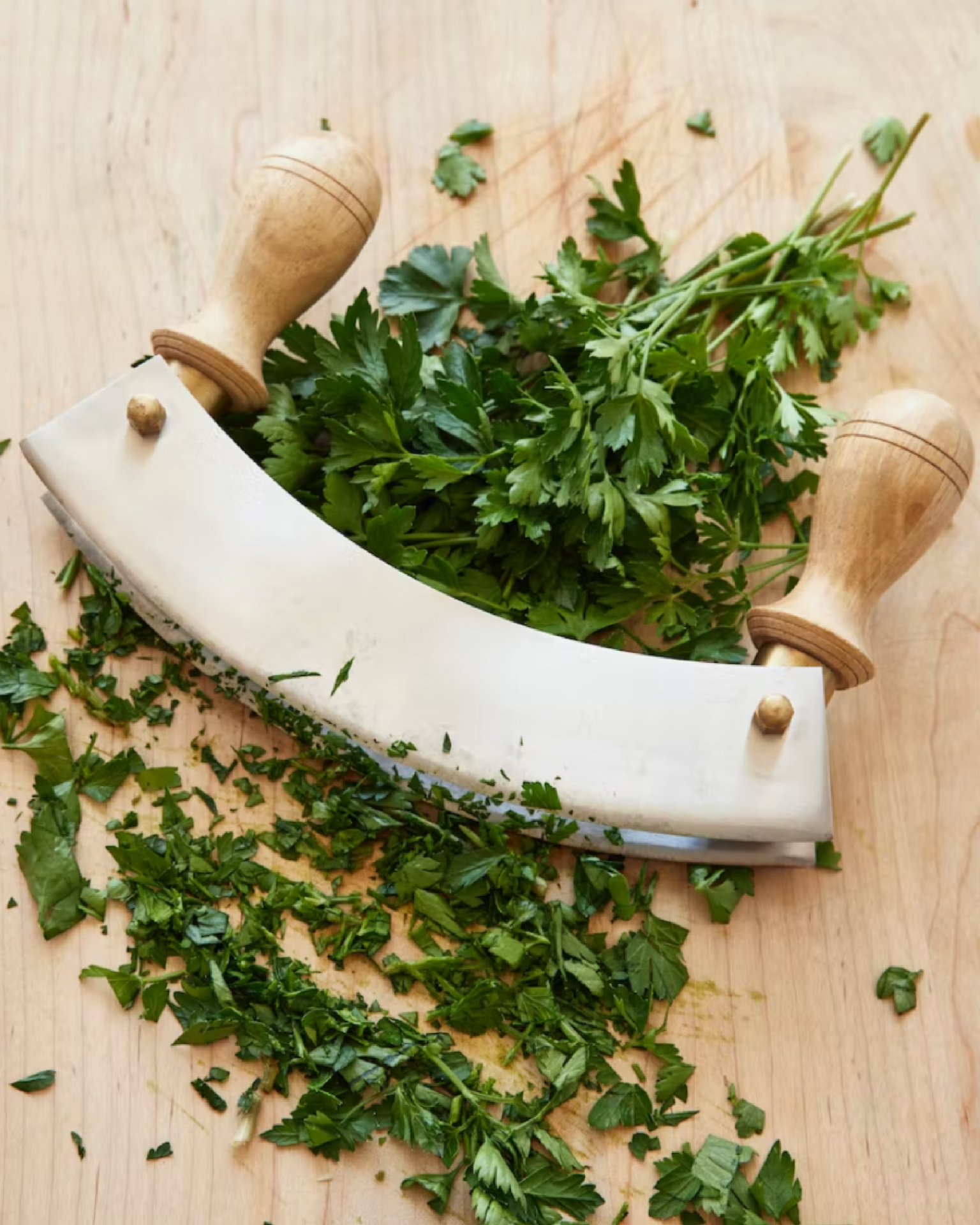 sir madam’s new double mezzaluna chopper on a wood cutting board with fresh herbs