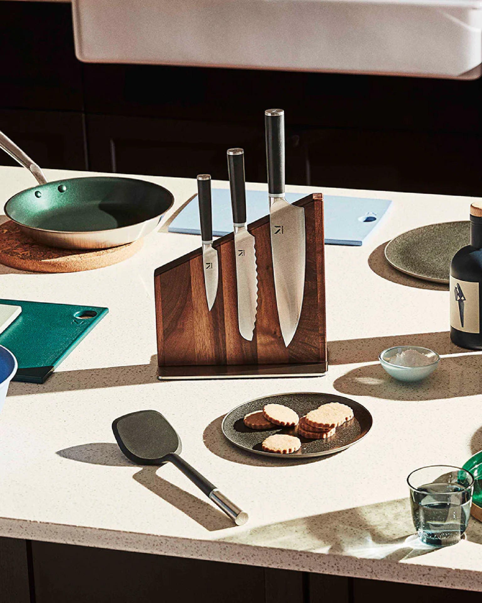 the trio of knives sorted vertically on a stand placed on a kitchen table with other kitchenwares