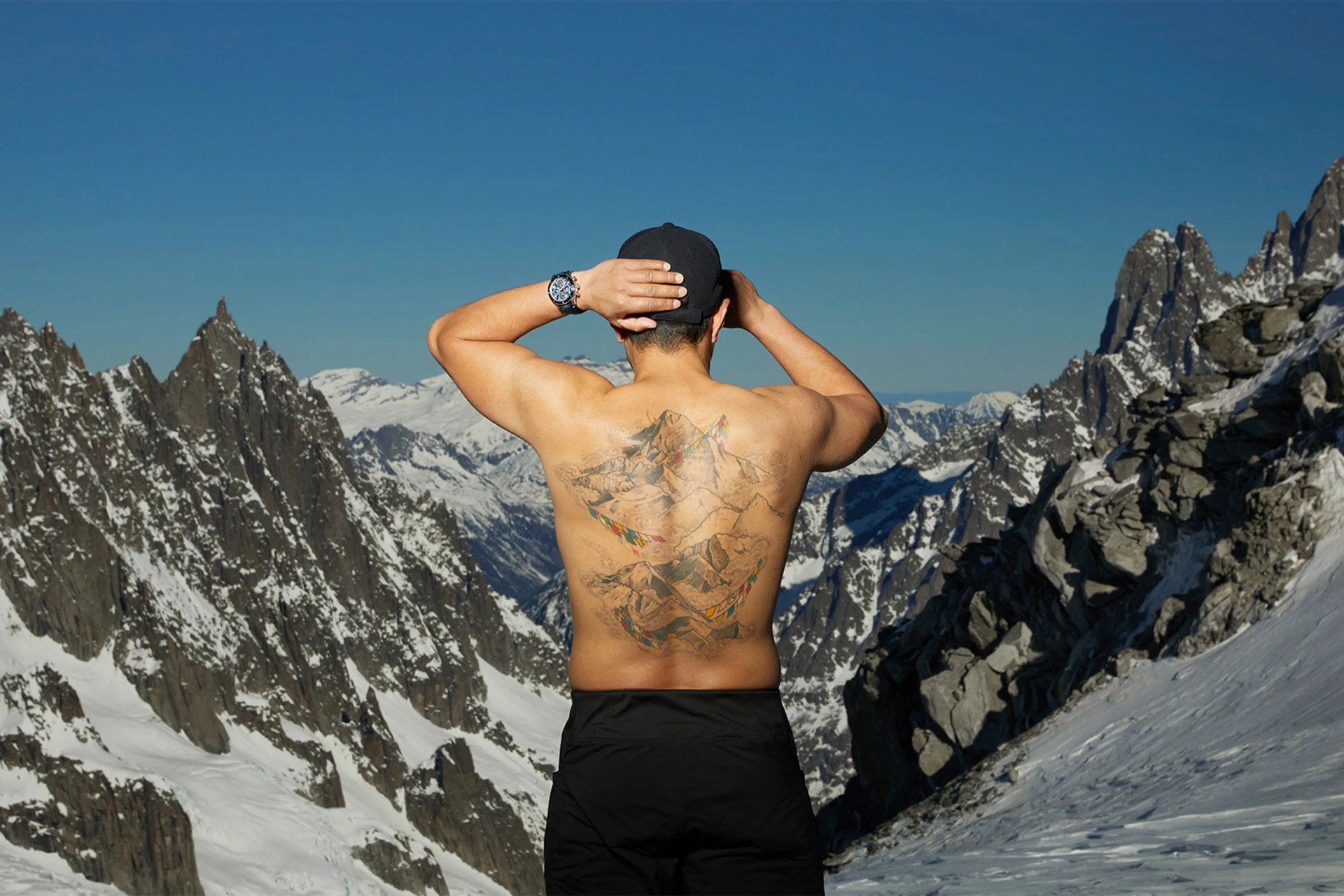 nimsdai purja showing his back tattoo overlooking a snowy mountain