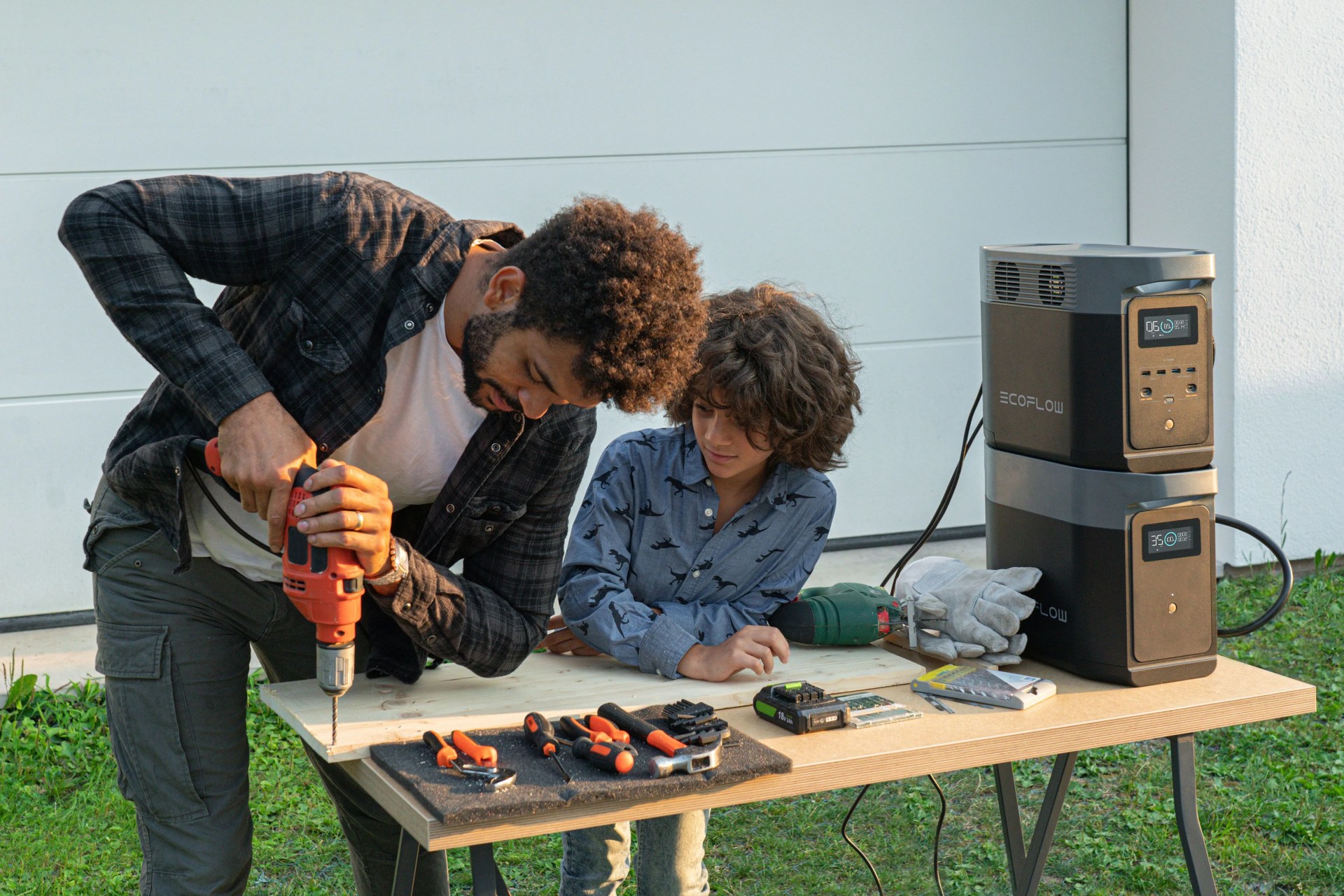 father drilling hole in wooden board using ecoflow power bank while son watches