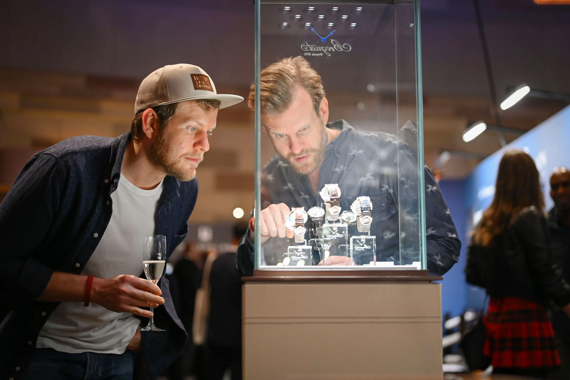 two men looking at watches in a case at a watch show