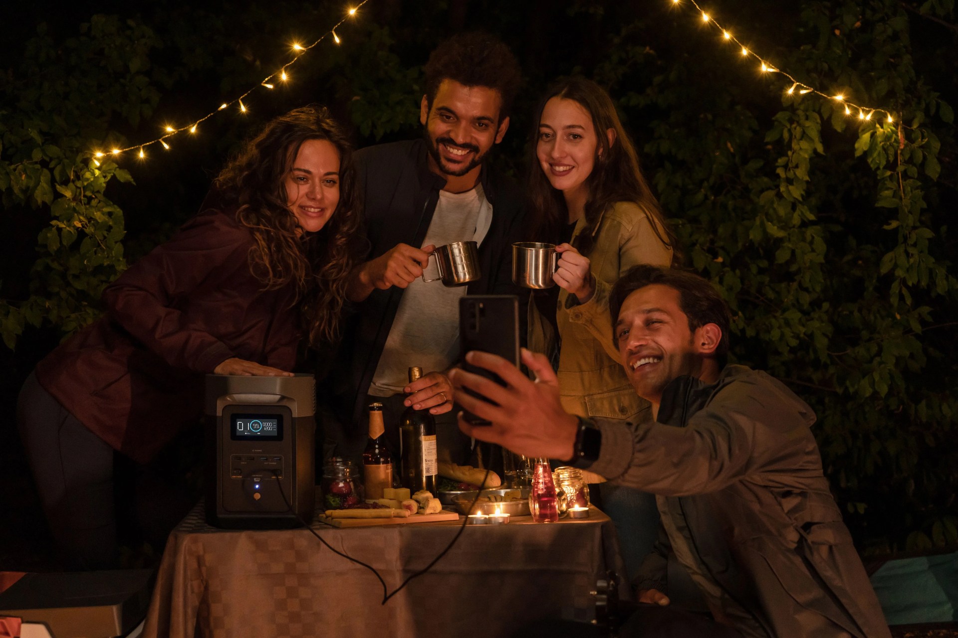 man using ecoflow delta 2 charger to charge his phone while taking a selfie with friends in backyard at night