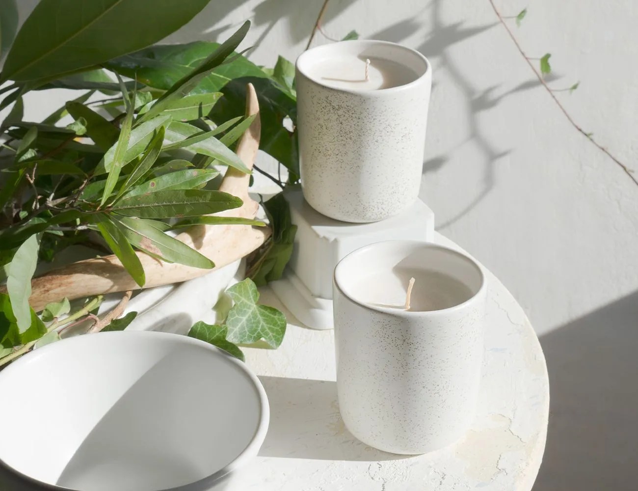 two candles on a table next to plants