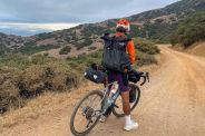 a man on a bike with bikepacking gear on a dirt road in the mountains