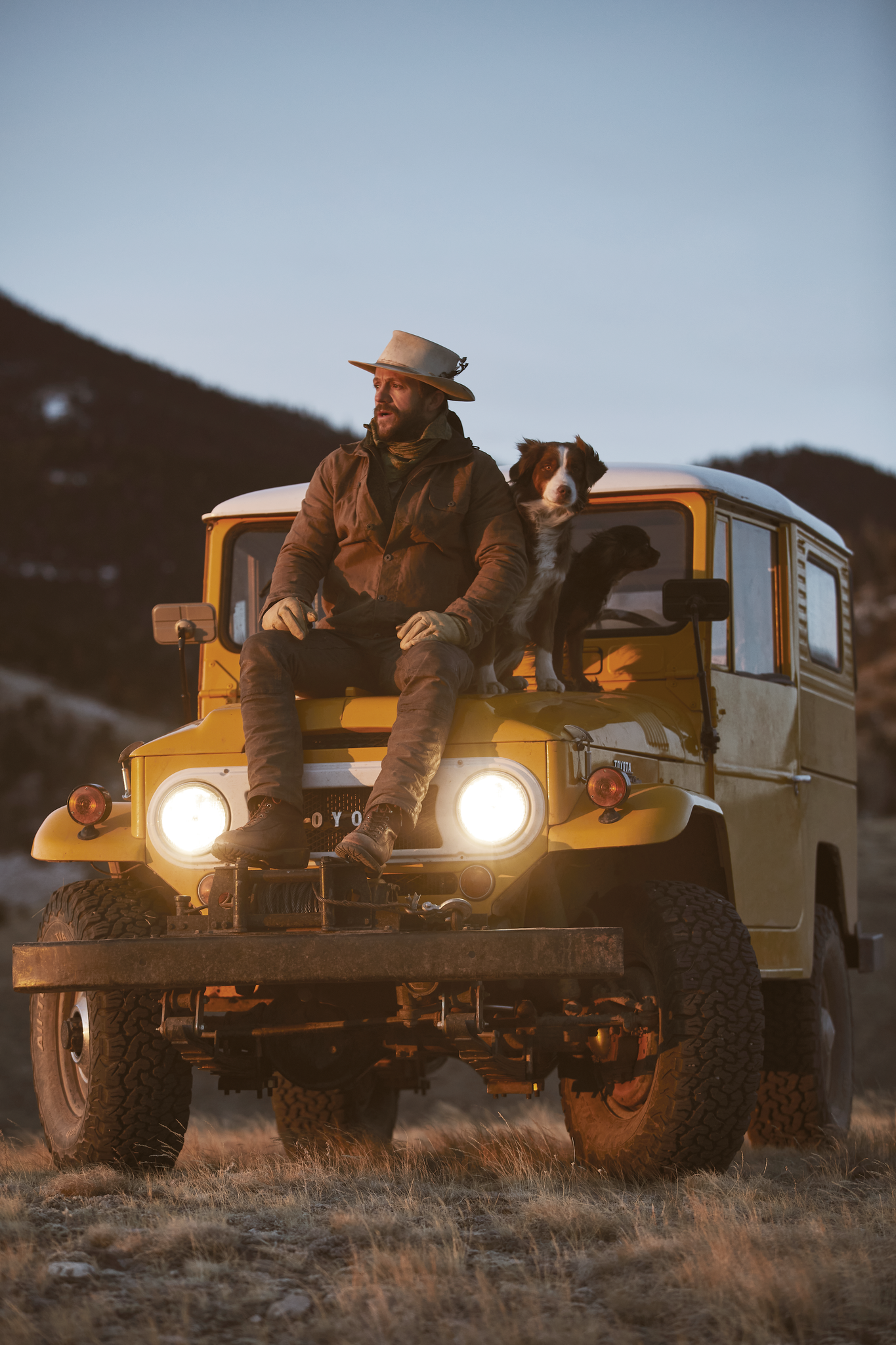 man wearing huckleberry gear sitting on car next to dog