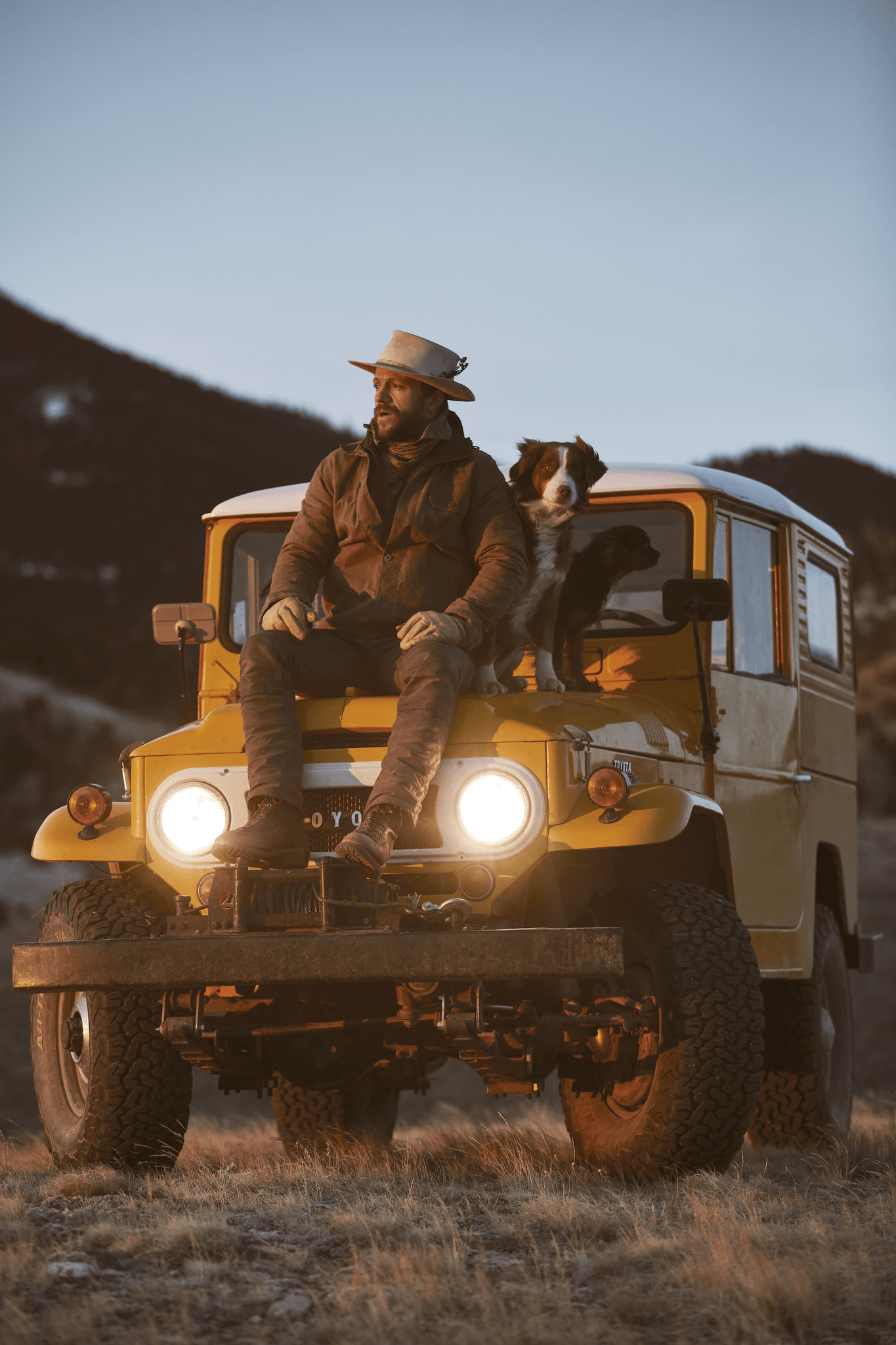 man wearing huckleberry gear sitting on car next to dog