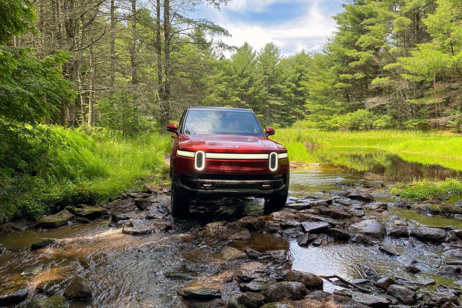 rivian r1s driving through a creek bed