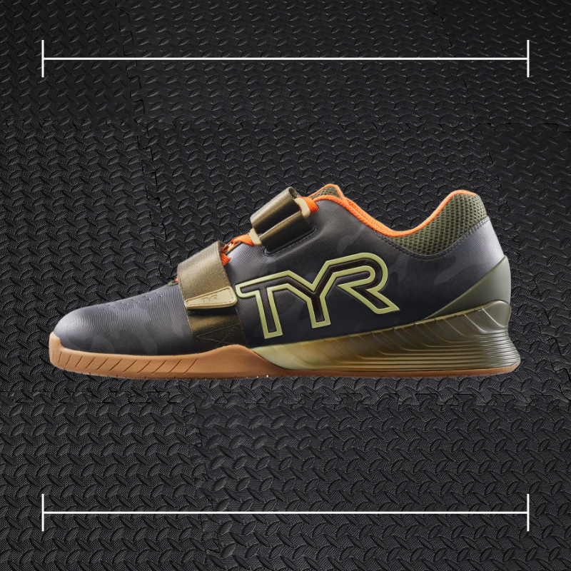 a black tyr fitness shoe with gum sole and orange and green accents laid overtop a photo of a black rubber gym floor
