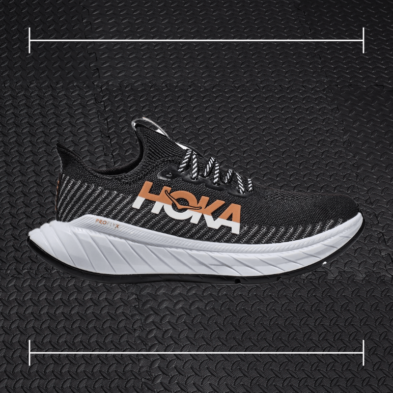 a black hoka fitness shoe with white sole and orange accents laid overtop a photo of a black rubber gym floor