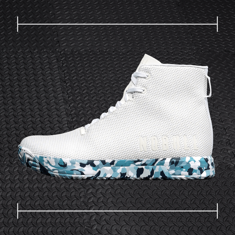 a white no bull fitness shoe with blue and black accents laid over top a photo of black rubber gym flooring
