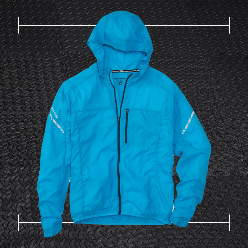 a blue nathan jacket laid on top of a photo of black rubber gym flooring